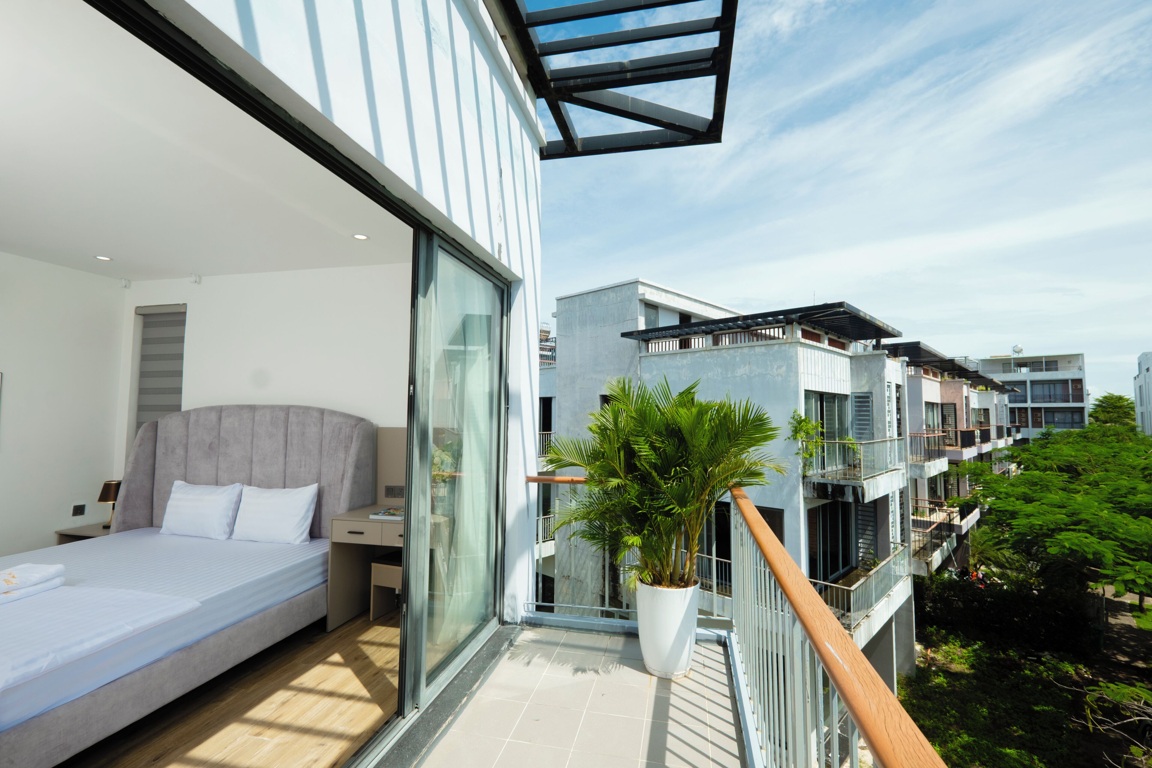 Quarto de hotel moderno com varanda, grandes janelas e vista para edifícios próximos.