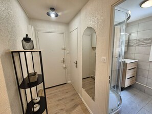 A bathroom with a glass shower enclosure, a white door, and a shelf with baskets and shoes. - Sleeps 4, Air conditioning, all on foot (ST MANDRIER SUR MER)