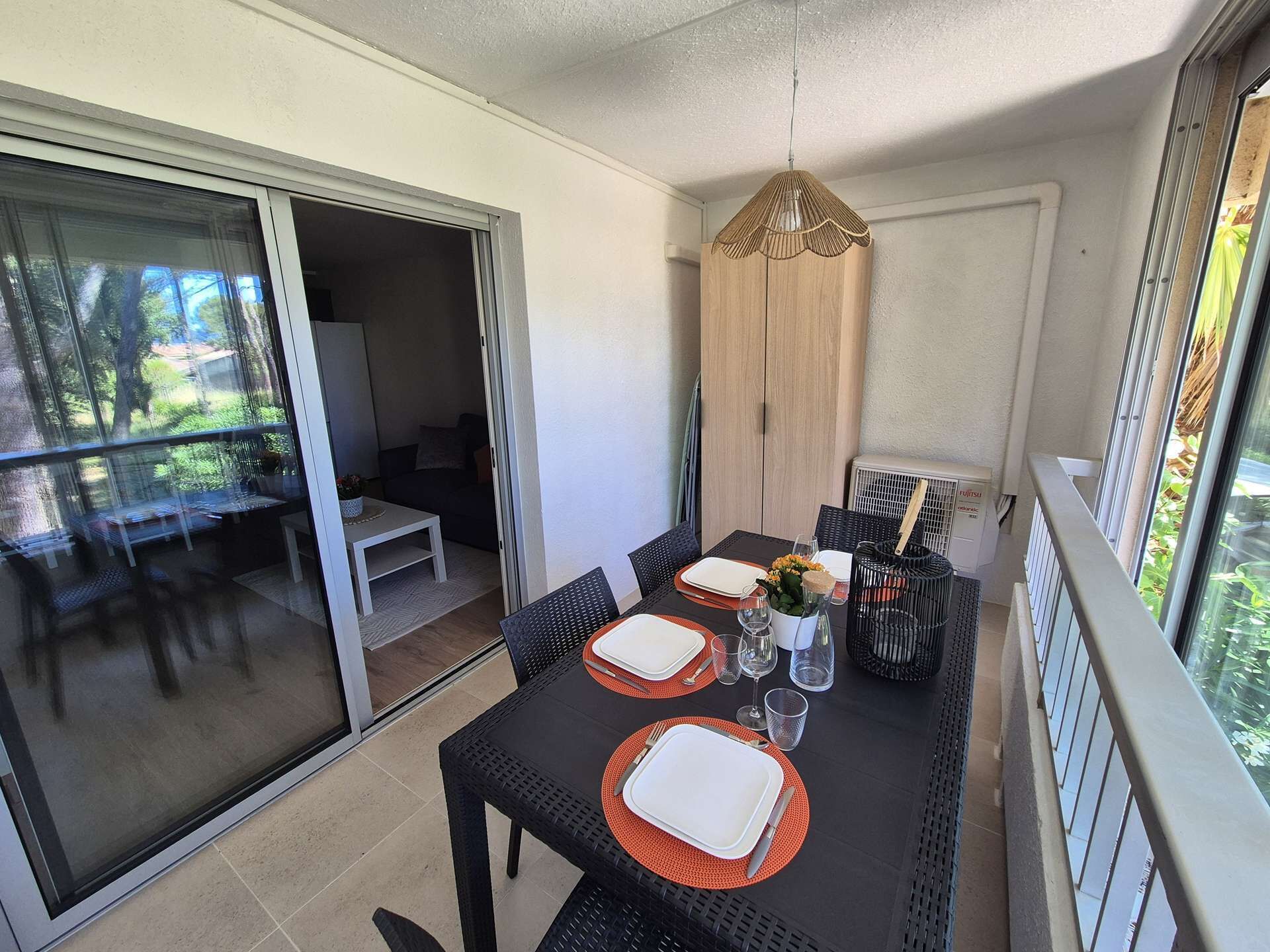 Un coin repas avec une table dressée pour quatre personnes, des portes-fenêtres coulissantes, un meuble en bois et un luminaire suspendu.