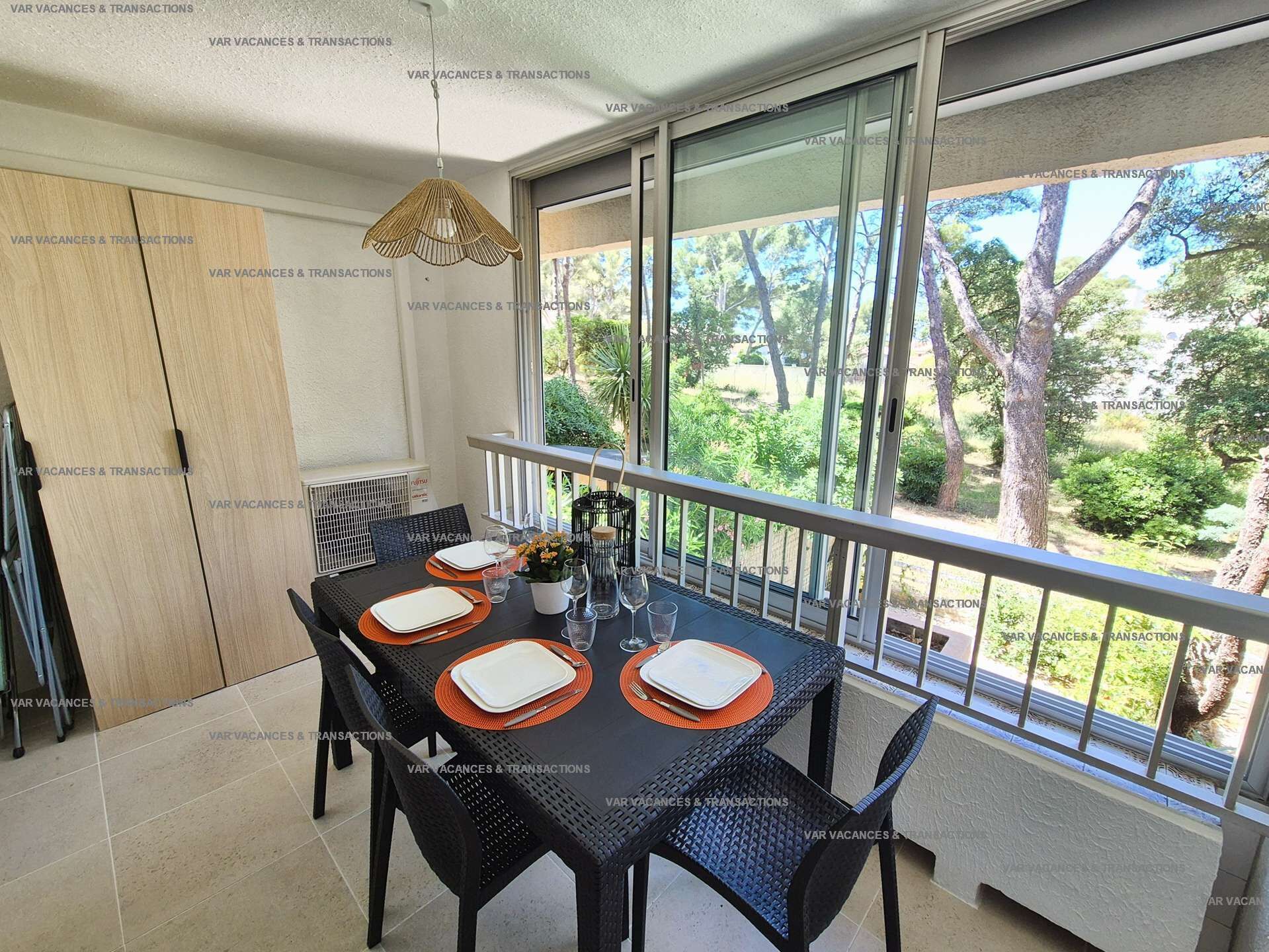 Un coin repas avec une table dressée pour quatre personnes, un luminaire suspendu et une vue sur la verdure à l’extérieur.