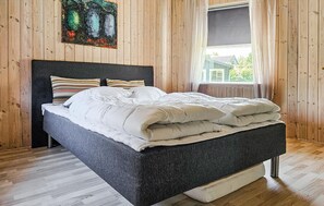 Un letto con testiera scura, biancheria bianca e cuscini a righe in una stanza con pareti in legno e una finestra.