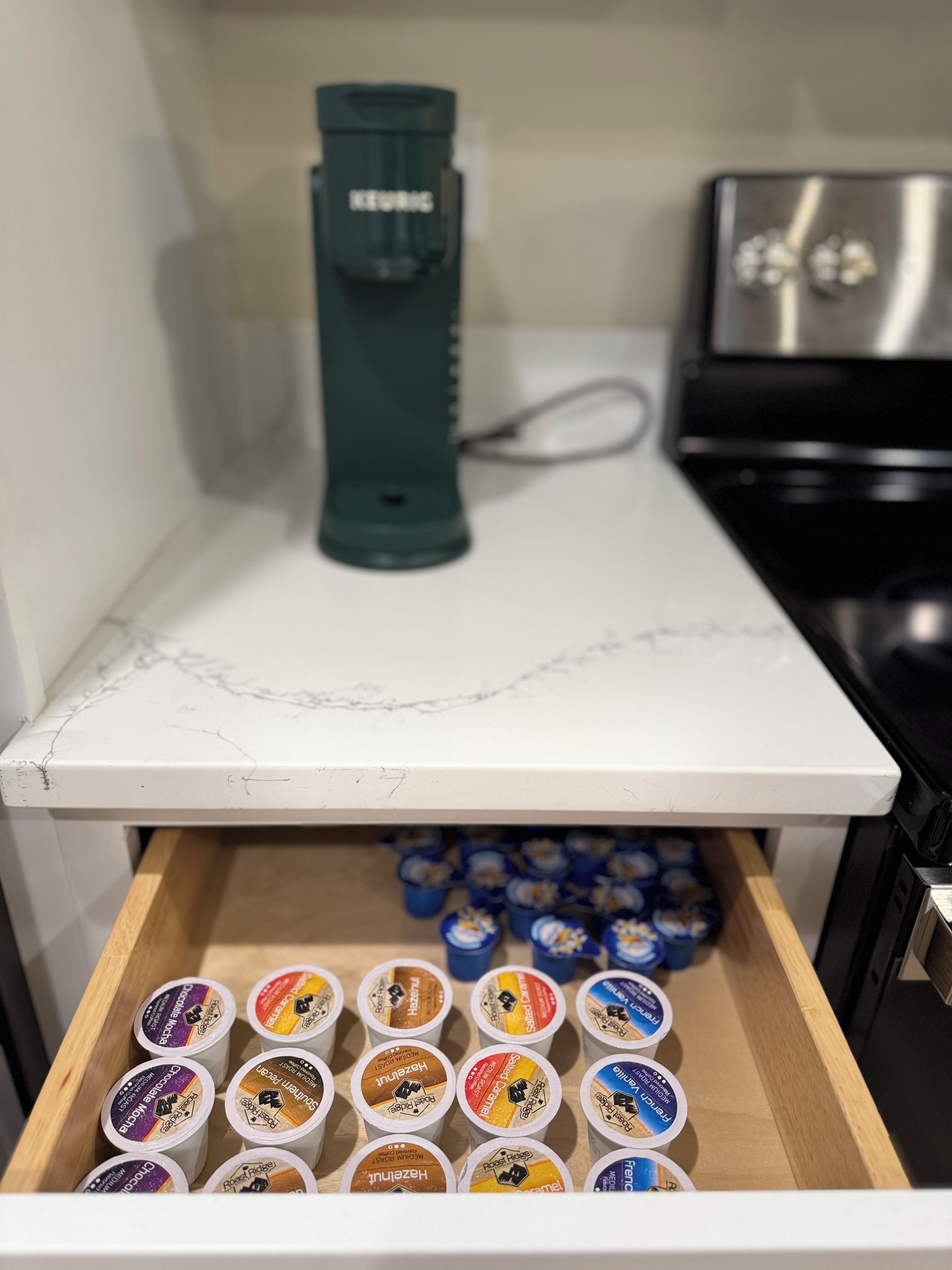 Una encimera de cocina con una cafetera y un cajón con varias cápsulas de café.