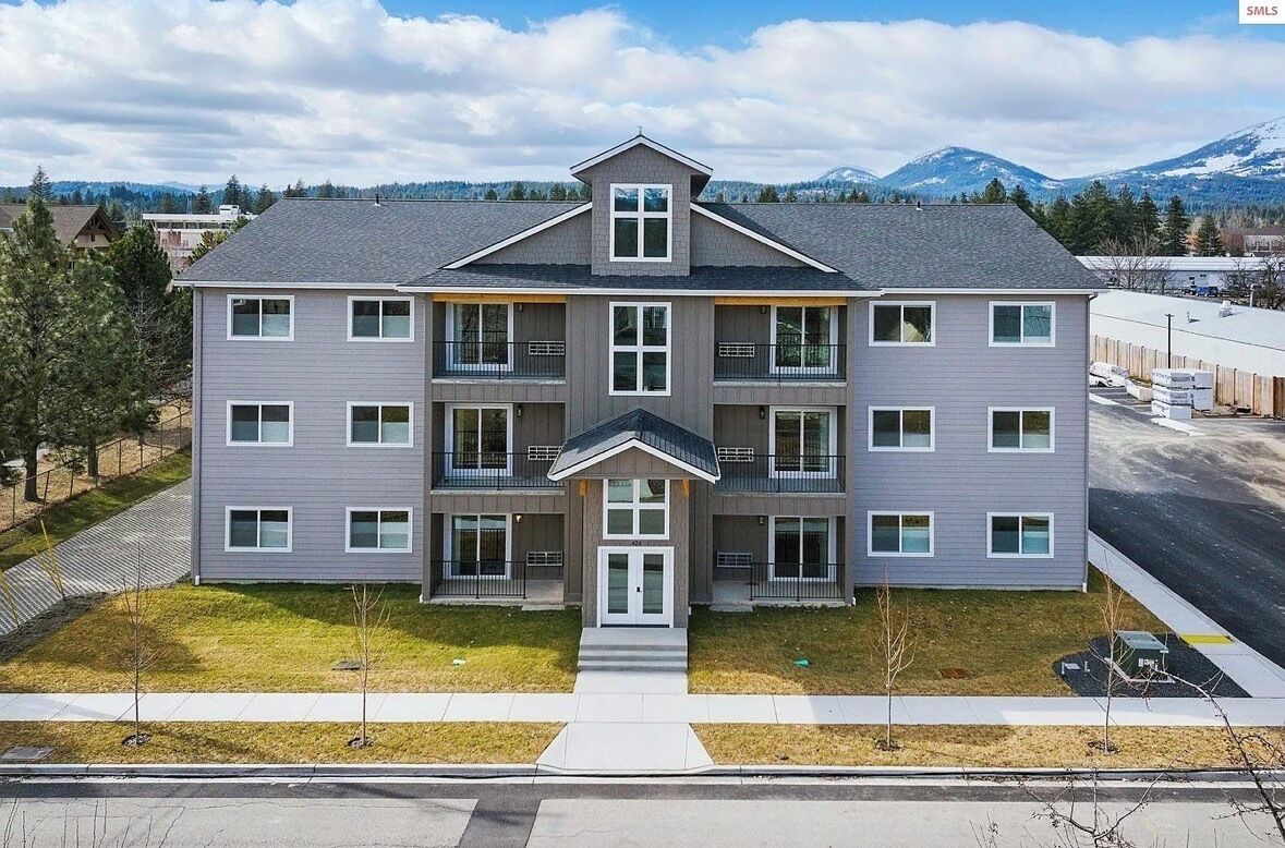 Un immeuble à plusieurs étages doté d’une entrée centrale, de balcons et offrant une vue sur les montagnes en arrière-plan.