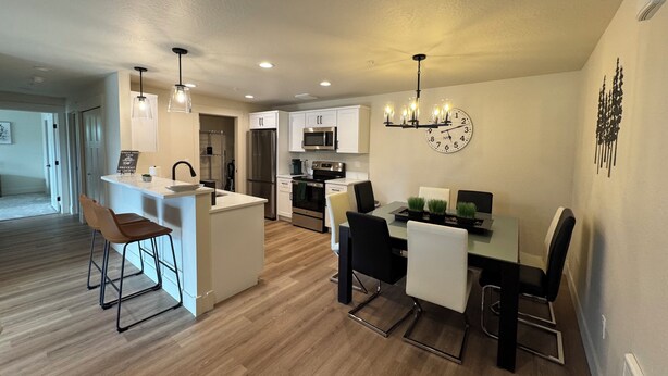 Una cocina moderna con armarios blancos, electrodomésticos de acero inoxidable y una zona de comedor con mesa y sillas.