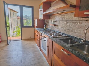 Eine Küche mit Steinrückwand, Holzschränken, einer Spüle aus Edelstahl und Blick durch eine Glastür.