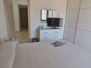 Ein Schlafzimmer mit Bett, Fernseher, einem kleinen Schminktisch und einer Mülltonne.