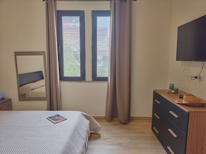 Una camera da letto con un letto, una cassettiera, una televisione e una finestra con tende.