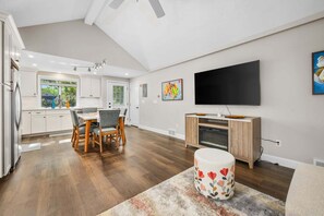 Eine moderne Küche mit weißen Schränken, ein Essbereich mit Stühlen, einem Flachbildfernseher und einem Kamin.
