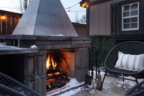 An outdoor stone fire pit with logs, surrounded by a wooden fence and a chair. - Alpine Elegance | Designer Main Floor (Calgary)