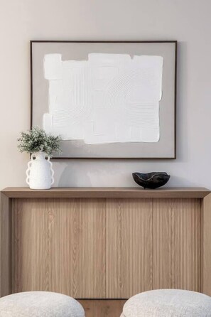 A framed abstract artwork on a wall, a white vase with a plant, and a dark bowl on a wooden shelf. - Alpine Elegance | Designer Main Floor (Calgary)