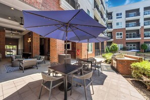 Un espace extérieur aménagé en terrasse, avec une table et des chaises, un grand parasol et un mur en briques.