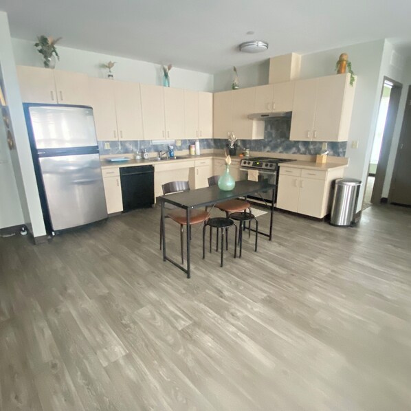 A modern kitchen with light wood cabinets, a stainless steel refrigerator, a dining table with chairs, and a small trash can. - Bright 2-bedroom apartment with AC in marvelous Nashville (Nashville)