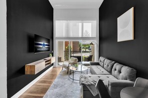 Un soggiorno moderno con una grande TV, un divano, un tavolino da caffè e vista panoramica attraverso una porta in vetro.