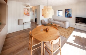 A modern living room with a round wooden table, two wicker chairs, a beige sofa, a television, and a large window. - Pet friendly home in Hvide Sande with sauna (Hvide Sande)