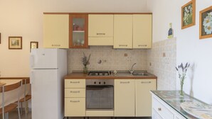 Eine kleine Küche mit Kühlschrank, Herd, Backofen, Spüle und Schränken.