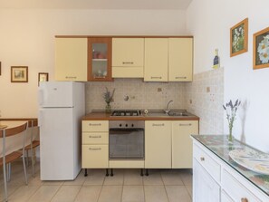 Eine kleine Küche mit Kühlschrank, Herd, Backofen, Spüle und Schränken.