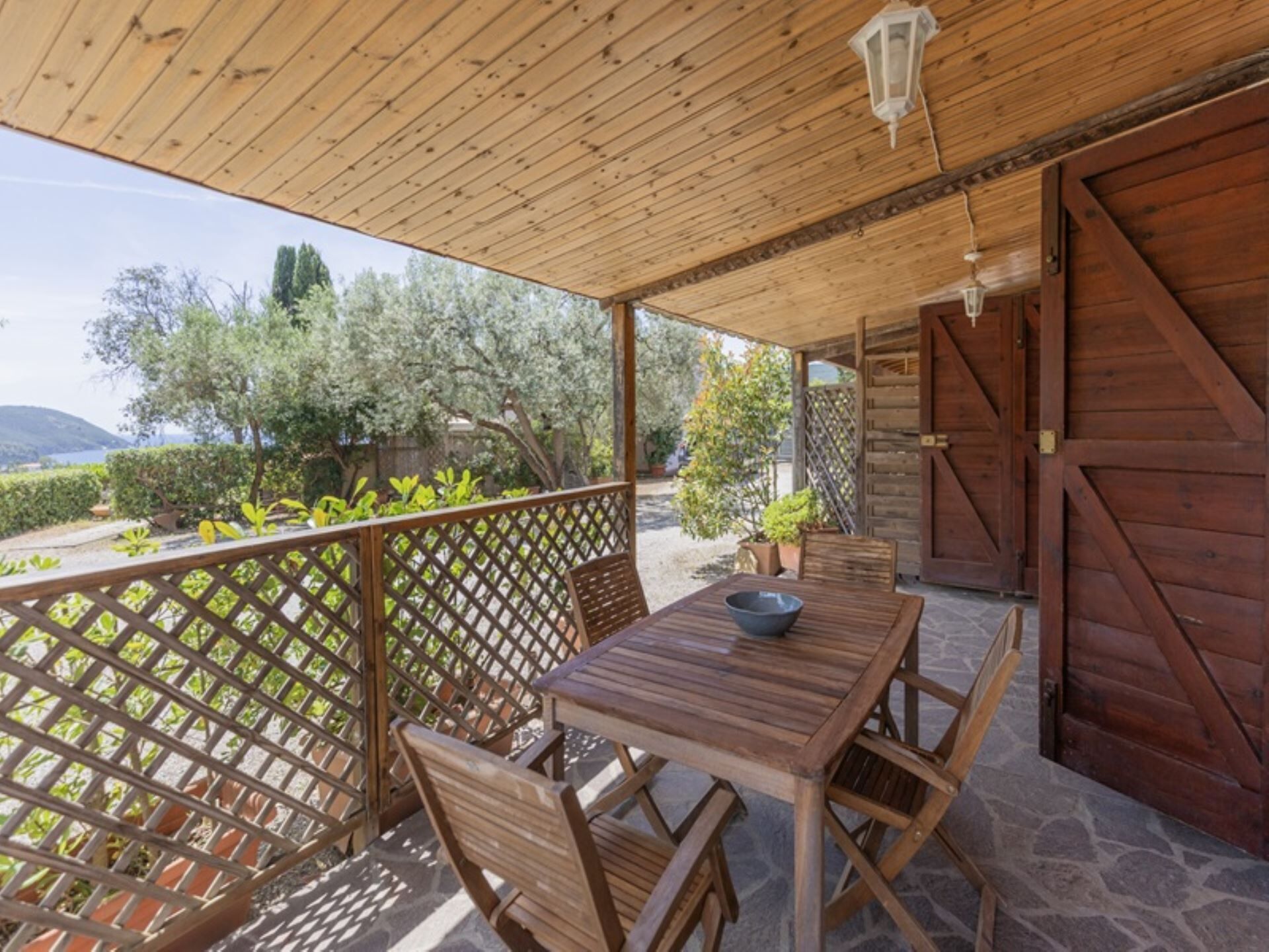 A wooden deck with a table and chairs, a wooden door, and a view of trees and hills.