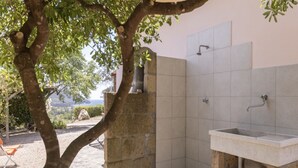 Ein Badezimmer aus Stein mit Waschbecken, Dusche und Blick ins Freie.