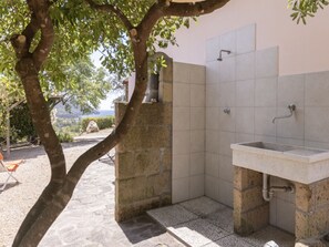 Ein Badezimmer aus Stein mit Waschbecken, Dusche und Blick ins Freie.