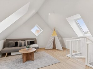 A loft bedroom with a sloped ceiling, a sofa, a round wooden coffee table, a white crib, a teepee, and skylights. - 4 Star Holiday Home in Skagen (Skagen)