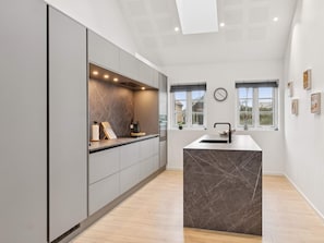 A modern kitchen with a marble island, built-in cabinets, and a large window providing natural light. - 4 Star Holiday Home in Skagen (Skagen)