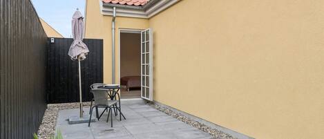 Une terrasse avec une table et des chaises, une clôture noire, un mur jaune et un toit recouvert de tuiles rouges.