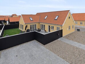 En gul byggnad med ett rött tegeltak, ett svart staket och en grusbelagd innergård.