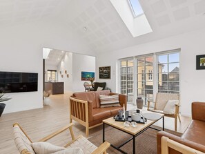 A spacious living area with a high ceiling, a large window, and a flat-screen TV mounted on the wall. - 4 Star Holiday Home in Skagen (Skagen)