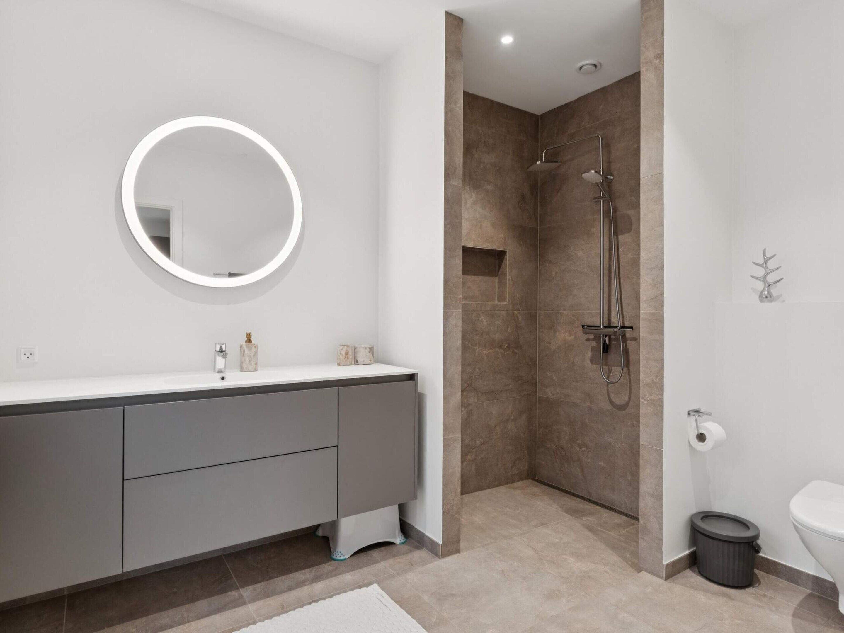 Een moderne badkamer met een ronde spiegel, een douche en een toilet.