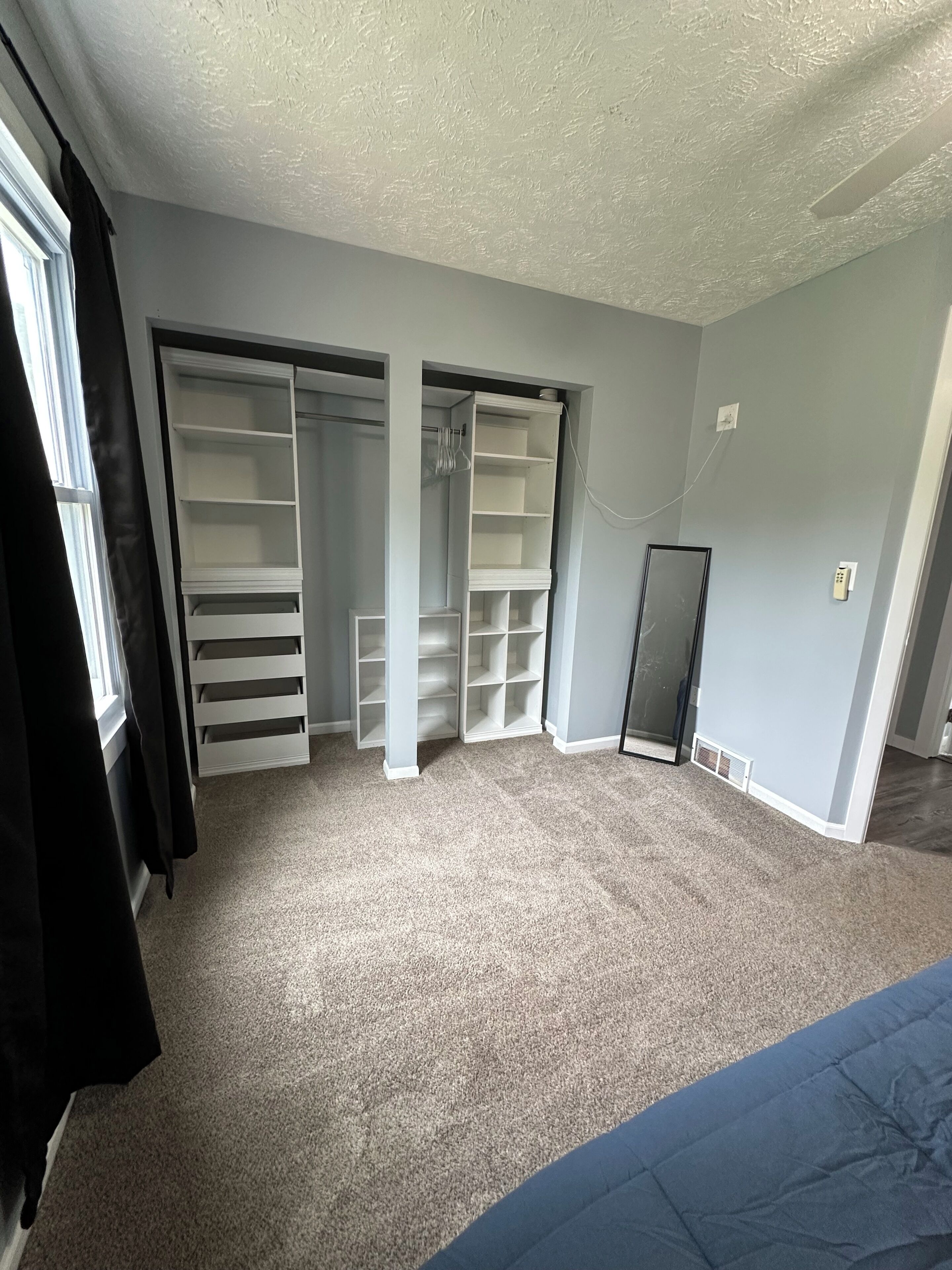 A room with a large closet, a radiator, and a window with curtains.