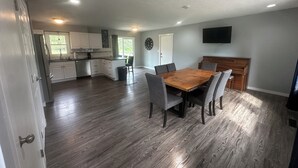 Un'ampia cucina con mobili bianchi, un'area pranzo con tavolo e sedie in legno e una TV a schermo piatto montata a parete.