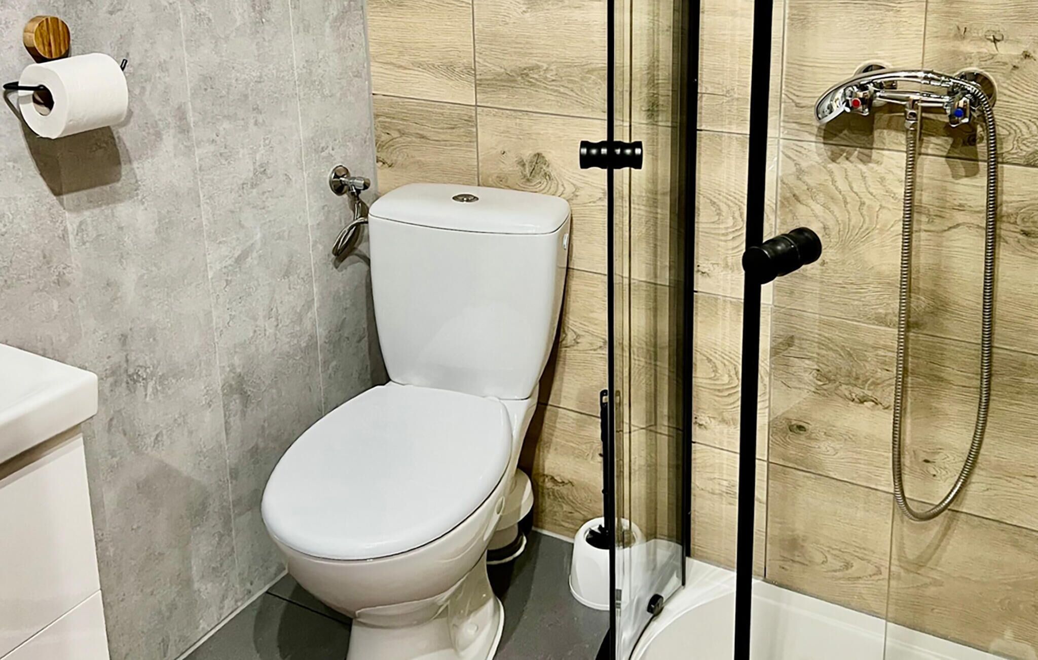 A modern bathroom with a toilet, shower, and a toilet paper holder on the wall.