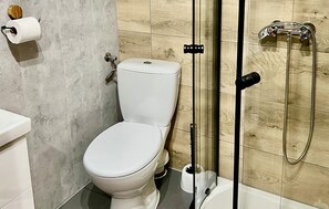Un baño moderno con inodoro, ducha y un dispensador de papel higiénico en la pared.