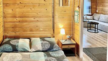 L’intérieur d’un chalet en bois comprend un lit, une table de chevet, une lampe et un canapé dans la pièce adjacente.