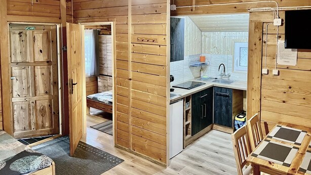 A wooden cabin interior with a kitchen, a dining area, and a bedroom.