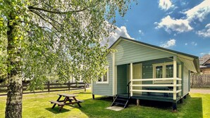 Eine kleine, eingeschossige Holzhütte mit Veranda, Picknicktisch und einem Rasen.