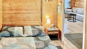 Ein Zimmer mit Holzboden, einem Bett, einem Nachttisch, einer Lampe und Blick auf einen anderen Raum mit Sofa und Tisch.