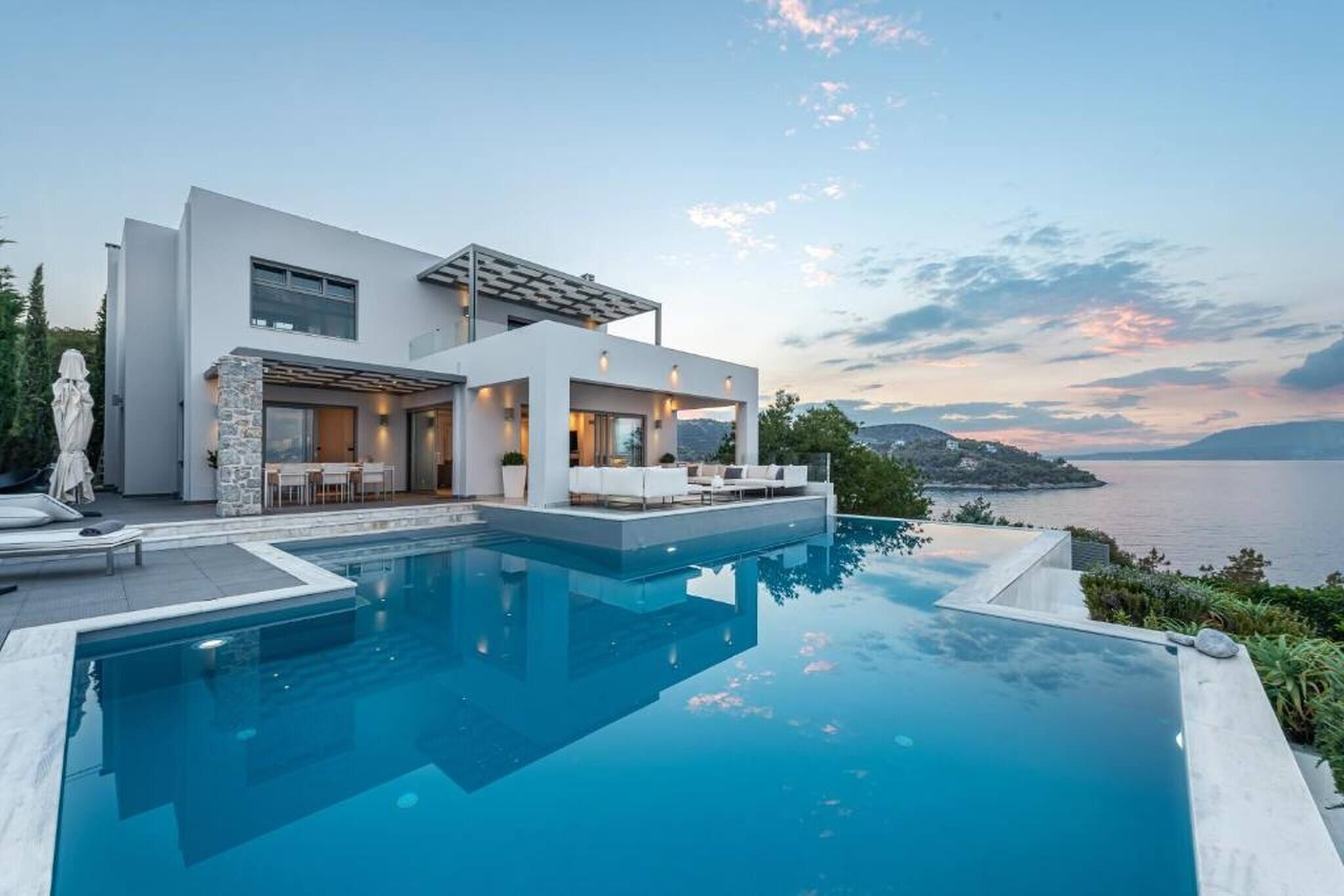 A modern two-story house with a swimming pool, outdoor seating, and a view of the sea.