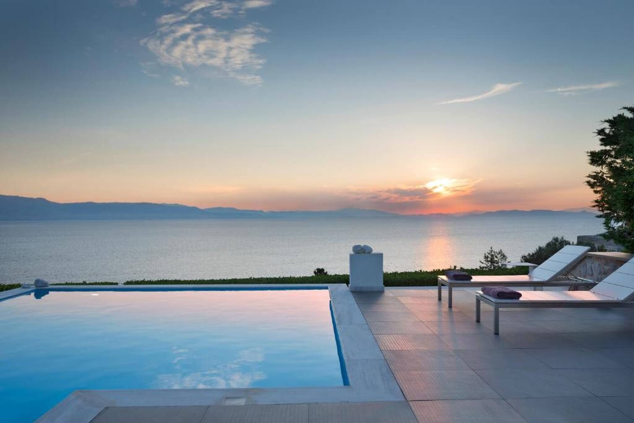 Une piscine à débordement offrant une vue sur la mer et les montagnes au coucher du soleil.