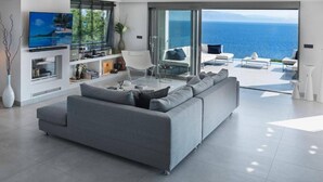 Ein modernes Wohnzimmer mit einem grauen Sofa, einem Flachbildfernseher und einem großen Fenster mit Meerblick.