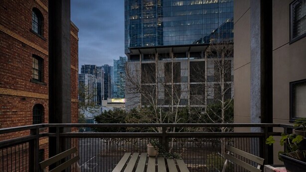 Un balcone con tavolo e due sedie, affaccia su un panorama urbano con edifici moderni.