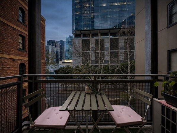 Ein Balkon mit Tisch und zwei Stühlen, mit Blick auf eine Skyline moderner Gebäude.