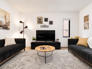 Un salon avec un canapé noir, une table basse, un téléviseur à écran plat et des objets décoratifs accrochés au mur.