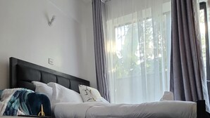 A bedroom with a bed, a bedside table, a patterned rug, and a window with curtains. - Delightful Executive Studio in Kiambu, family friendly and relaxing. (Kiambu Province)