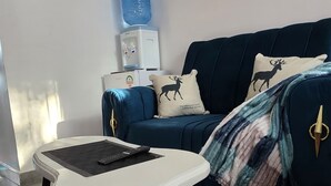 A room with a white table, a dark blue sofa, a patterned rug, and a water dispenser on the wall. - Delightful Executive Studio in Kiambu, family friendly and relaxing. (Kiambu Province)