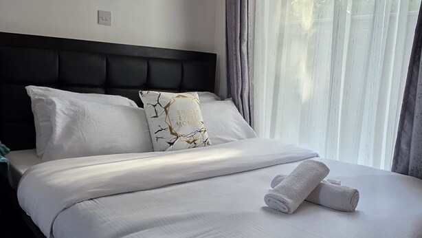 A neatly made bed with white linens, a headboard, and two rolled towels. - Delightful Executive Studio in Kiambu, family friendly and relaxing. (Kiambu Province)