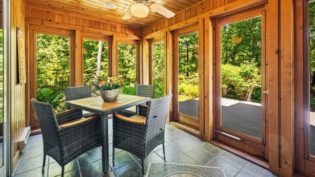 A wooden-paneled room with a table and chairs, large windows, and a ceiling fan.