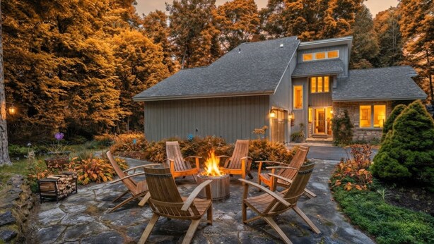 Ein Haus mit einer Steinterrasse, Sitzgelegenheiten im Freien und einer Feuerstelle.