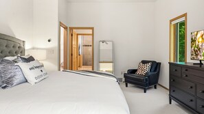 A bedroom with a bed, a dresser, a chair, a mirror, and a television.