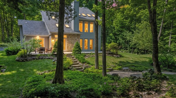A modern house with a stone exterior, large windows, and a well-maintained garden with a stone pathway leading to the entrance.